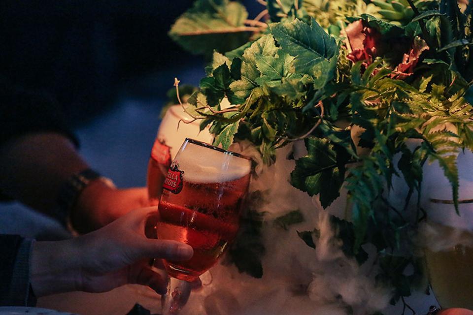 Un invité tient une bière Stella Artois à côté d'un centre de table floral luxuriant avec des effets de brume lors d'un dîner expérimental organisé par le Cirque du Soleil.