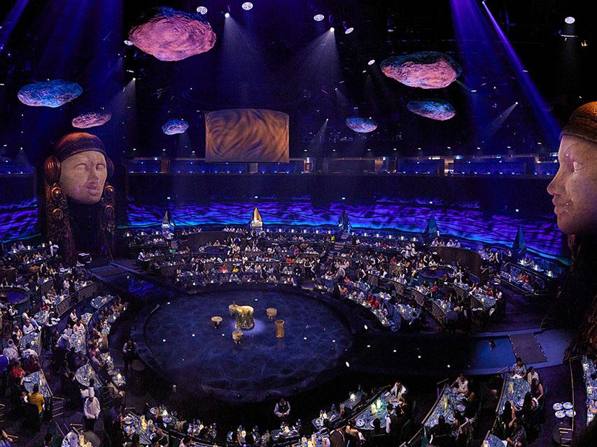 La scène du spectacle LUDO du Cirque du Soleil à Nuevo Nayarit, avec un grand théâtre aquatique, un éclairage immersif et des sièges pour le public entourant la scène.