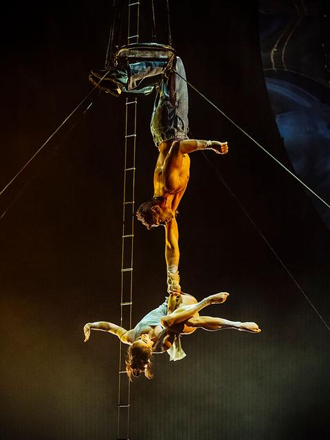 Le duo aérien du Cirque du Soleil exécute une figure acrobatique inversée suspendu à une échelle au-dessus de la scène.