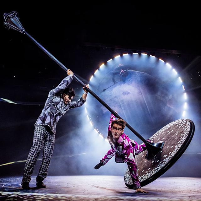 Les artistes du Cirque du Soleil font des figures d'équilibre et tournent sur un grand poteau rotatif et un disque sous un éclairage spectaculaire.
