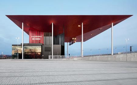 Vue extérieure de l'amphithéâtre Cogeco à Trois-Rivières, avec son toit rouge saisissant et sa place publique, photographié à la lumière du jour.