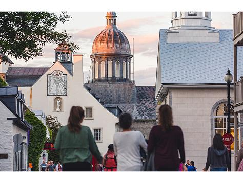 Les visiteurs marchent dans la rue Trois-Rivières vers un bâtiment emblématique au dôme, au coucher du soleil.